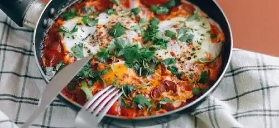A skillet of shakshouka with a knife and fork-min