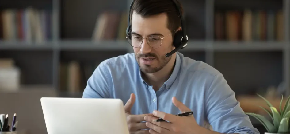 Confident man teacher coach wearing headset speaking, holding online lesson, focused student wearing glasses looking at laptop screen, studying, watching webinar training, listening to lecture