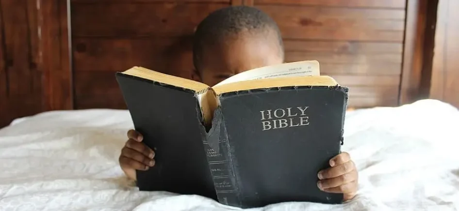 Child reading bible in bed